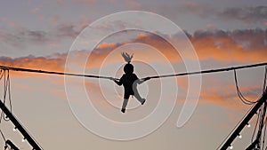 Girl silhouette is jumping on bungee trampoline against twilight sky: slow mo
