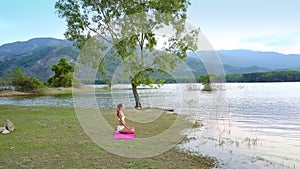 Girl silhouette sits in yoga pose at tree watches lake hills