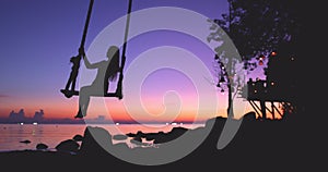 Girl silhouette swing enjoys bright ocean sunset