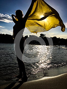 Girl silhouette with yellow scarf under sunset