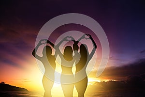 girl silhouettes hands making heart shape with sunset background