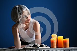 Girl in silver wig posing with book and candles. Close up. Blue background