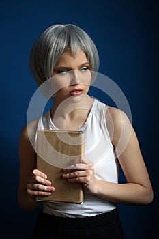 Girl in silver wig posing with book. Close up. Blue background