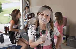 Girl Singing Into Microphone With Friends Playing Musical Instrument
