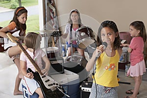 Girl Singing Into Microphone With Friends Playing Musical Instrument