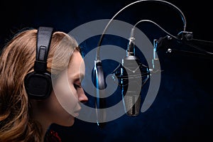 Girl singer sings into a microphone, with a spectacular background, vocals, recording studio, recording a track. On a black photo