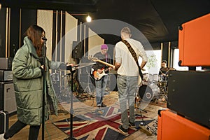 A girl sings into a microphone, two guys play an electric guitar. Band rehearsing a performance
