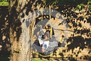 A girl sits alone in a comfy hammock reading a book during a warm sunny evening garden