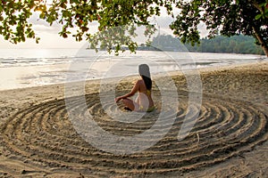 The girl sits back on the sandy beach in the center of an impromptu circle and meditates