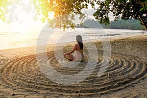 The girl sits back on the sandy beach in the center of an impromptu circle and meditates