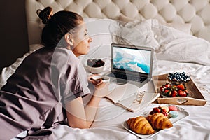 A girl sits in bed in the evening, with a smartphone in her hand and eats strawberries, a girl in bed has sweets before going to