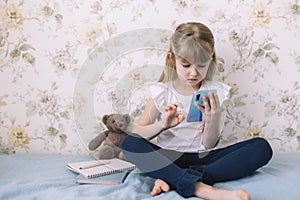 Girl sits on bed, holding phone and reads something in smartphone