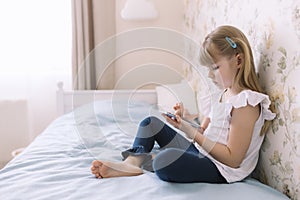 Girl sits on bed, holding phone and reads something in smartphone