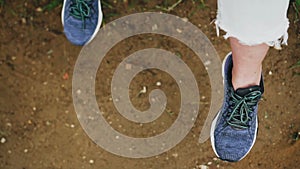 The girl sits on the bench with her legs hanging down and moves her legs. Close-up from above