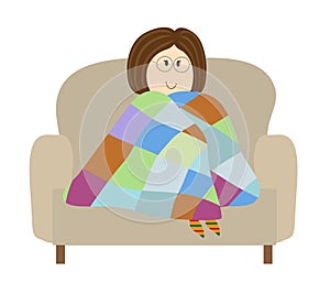 The girl sits in a chair and basks in the blanket.