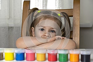 the girl sits on a chair and spread multicolored oil paints in front of her