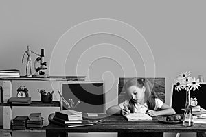 Girl sits at desk with books, flowers, fruit and blackboard