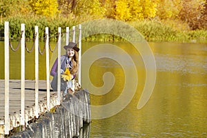 Girl sits on a dock near the water in a hat and with leaves in h