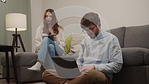 The girl sits down next to the man with the computer and she looks at the iPad.