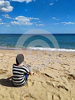 Girl sits on an empty beach and looks at the sea, back view