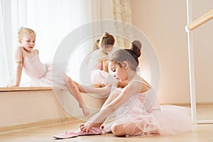 Girl sits on the floor. Little ballerinas preparing for performance by practicing dance moves