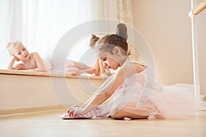 Girl sits on the floor. Little ballerinas preparing for performance by practicing dance moves