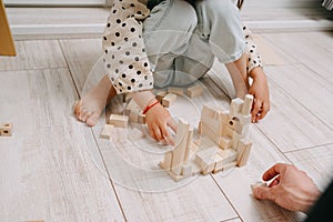 Girl sits on the floor and plays a wooden constructor with her dad. Eco-toys.