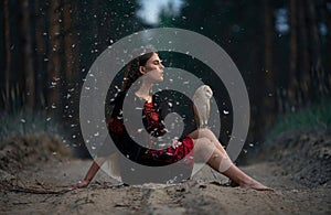 Girl sits on forest road with owl on her knees among flying fluff .