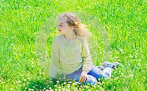 Girl sits on grass at grassplot, green background. Child enjoy spring sunny weather while sitting at meadow. Springtime