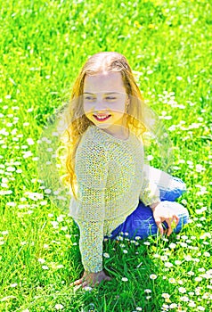 Girl sits on grass at grassplot, green background. Heyday concept. Girl on smiling face spend leisure outdoors. Child photo