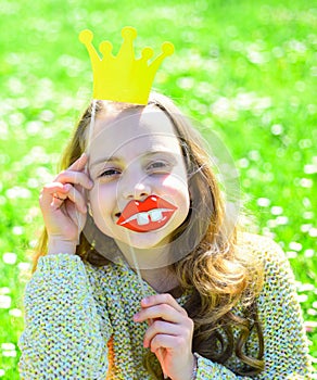 Girl sits on grass at grassplot, green background. Sweet little girl with crown, outdoor photo. Humour queen concept