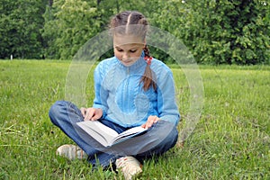 Girl sits on green field and reads book photo