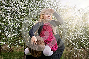 The girl sits on her fatherâ€™s shoulders in the sun. Against the background of a blooming garden. A happy family