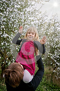 The girl sits on her fatherâ€™s shoulders in the sun. Against the background of a blooming garden. A happy family