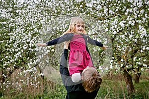 The girl sits on her fatherâ€™s shoulders in the sun. Against the background of a blooming garden. A happy family