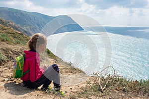 The girl sits on high bank and looks at the sea