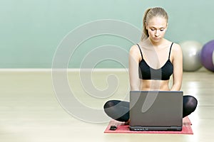 Girl sits with the laptop in sports gym