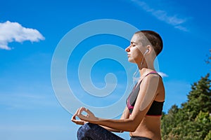 Girl sits in lotus position on beach and meditates on sunny day listening