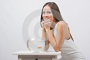 The girl sits near the aquarium with goldfish and looks in the picture