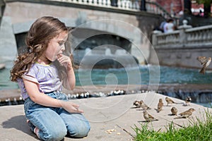 Girl sits near the fountain eating cookies and feeding birds