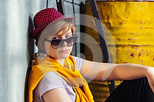 A girl sits near an yellow metal barrel