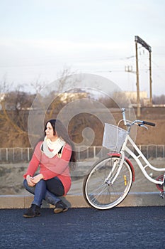 The girl sits next to a parked bike. Rest on the spring cycle