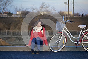 The girl sits next to a parked bike. Rest on the spring cycle