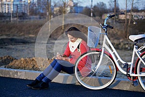 The girl sits next to a parked bike. Watching something on the phone. Rest on the spring cycle