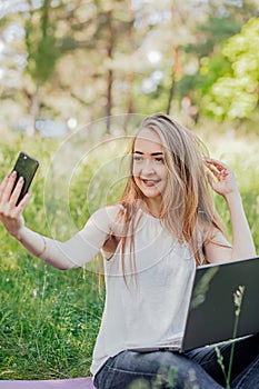 girl sits outdoors and works at a laptop. makes a selfie on the phone. freelance. selfeducation. the concept of remote photo