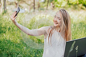 girl sits outdoors and works at a laptop. makes a selfie on the phone. freelance. selfeducation. the concept of remote photo