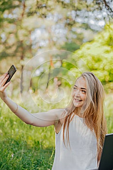 girl sits outdoors and works at a laptop. makes a selfie on the phone. freelance. selfeducation. the concept of remote photo