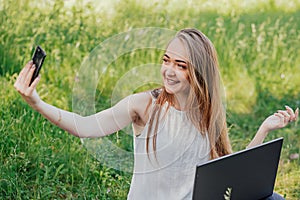 girl sits outdoors and works at a laptop. makes a video call on the phone. freelance. selfeducation. the concept of photo