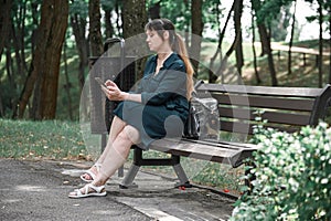 A girl sits on a park bench and looks at her phone, waiting for a man on a date