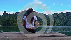 A girl sits on a pier in a lotus pose on a lake with a beautiful view.